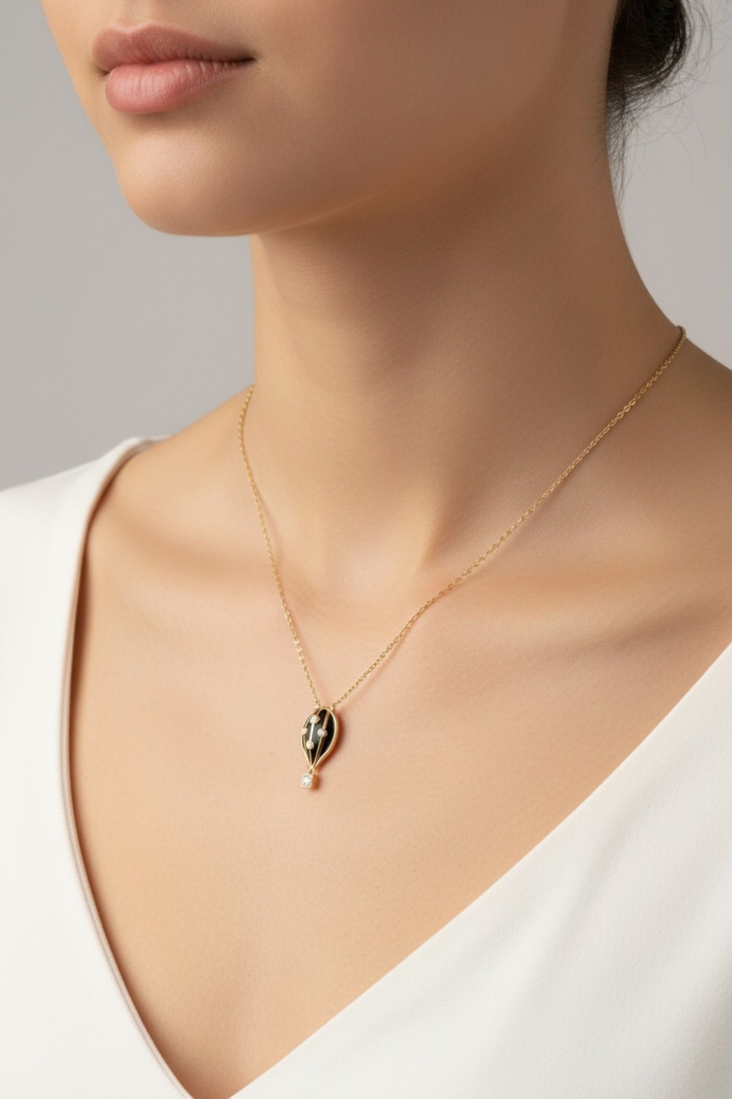 Necklace with a black hot air balloon pendant worn by a person against a neutral background