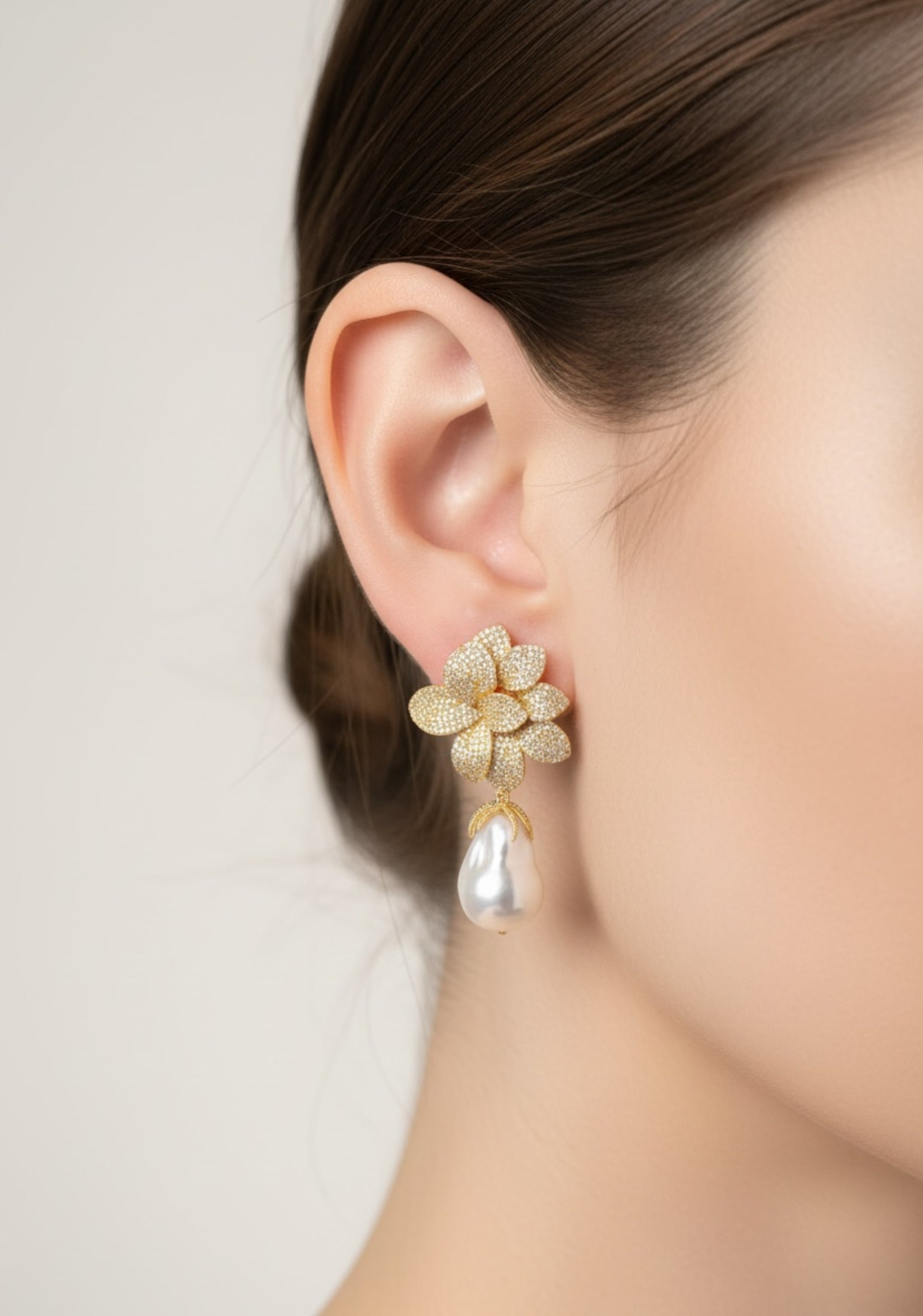 Gold floral earring worn by a person on a plain background