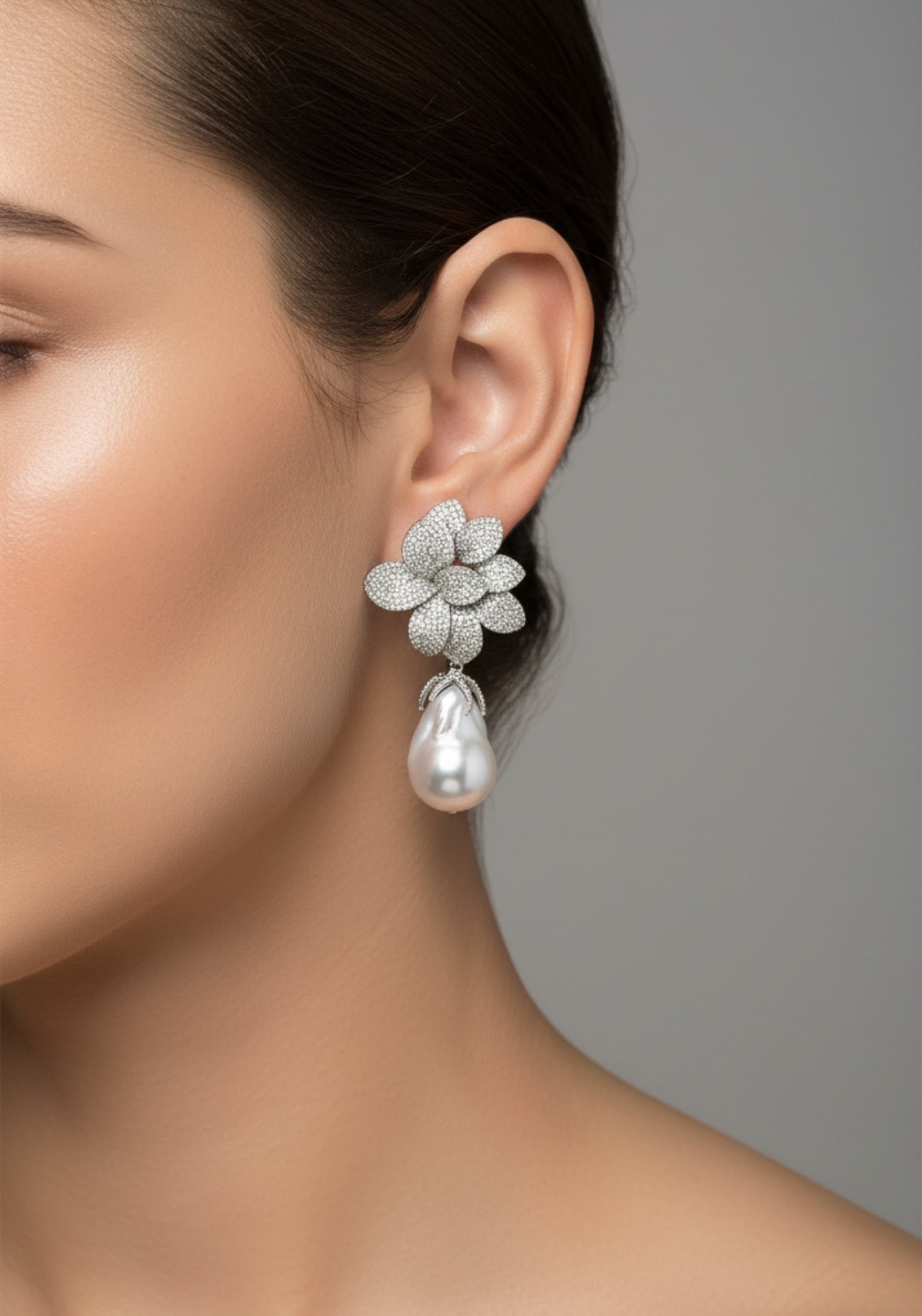 Close-up of a woman wearing a floral earring with a pearl drop on a gray background