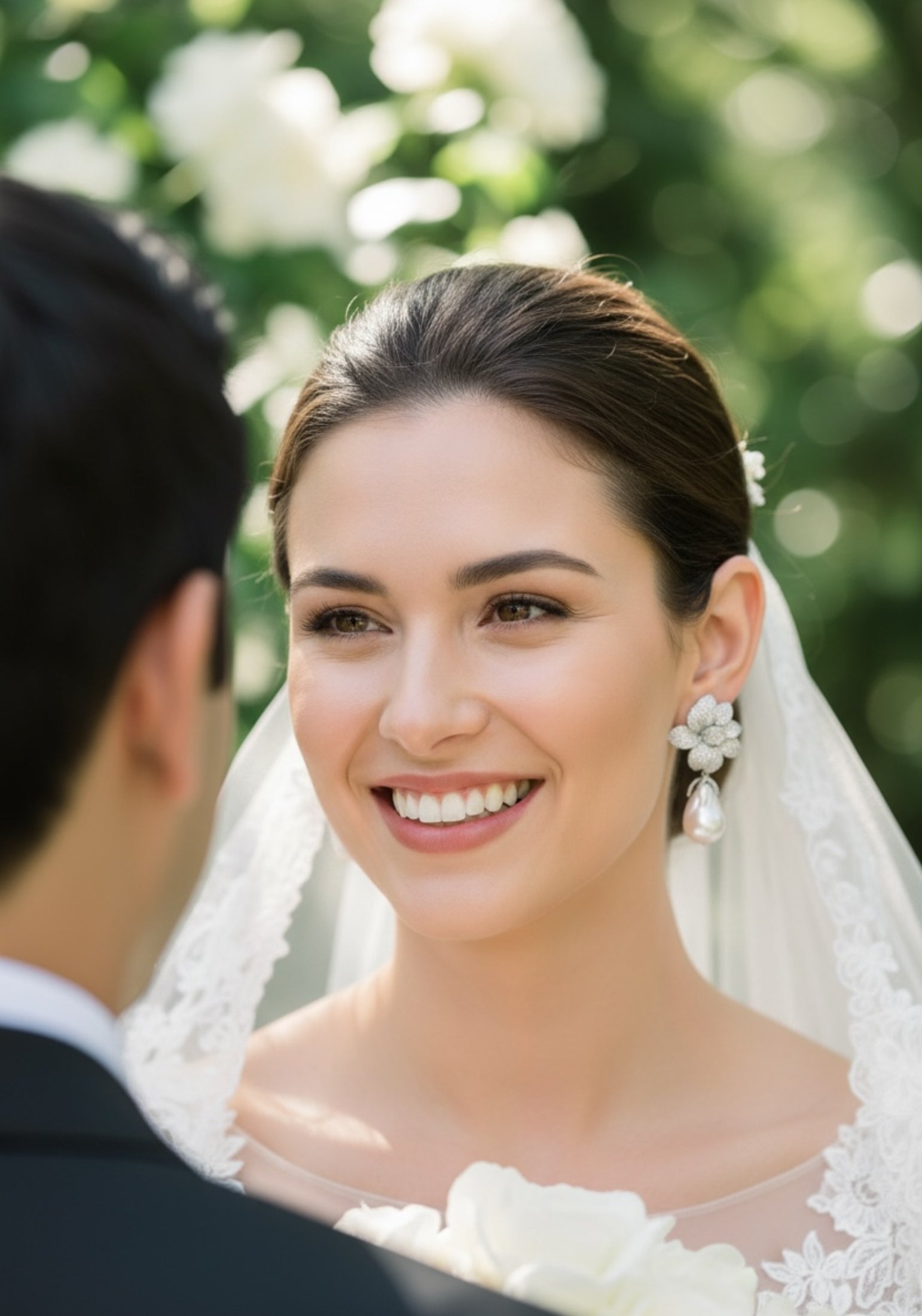 Woman in a wedding dress smiling at a man outdoors wearing silver floral pearl drop earrings
