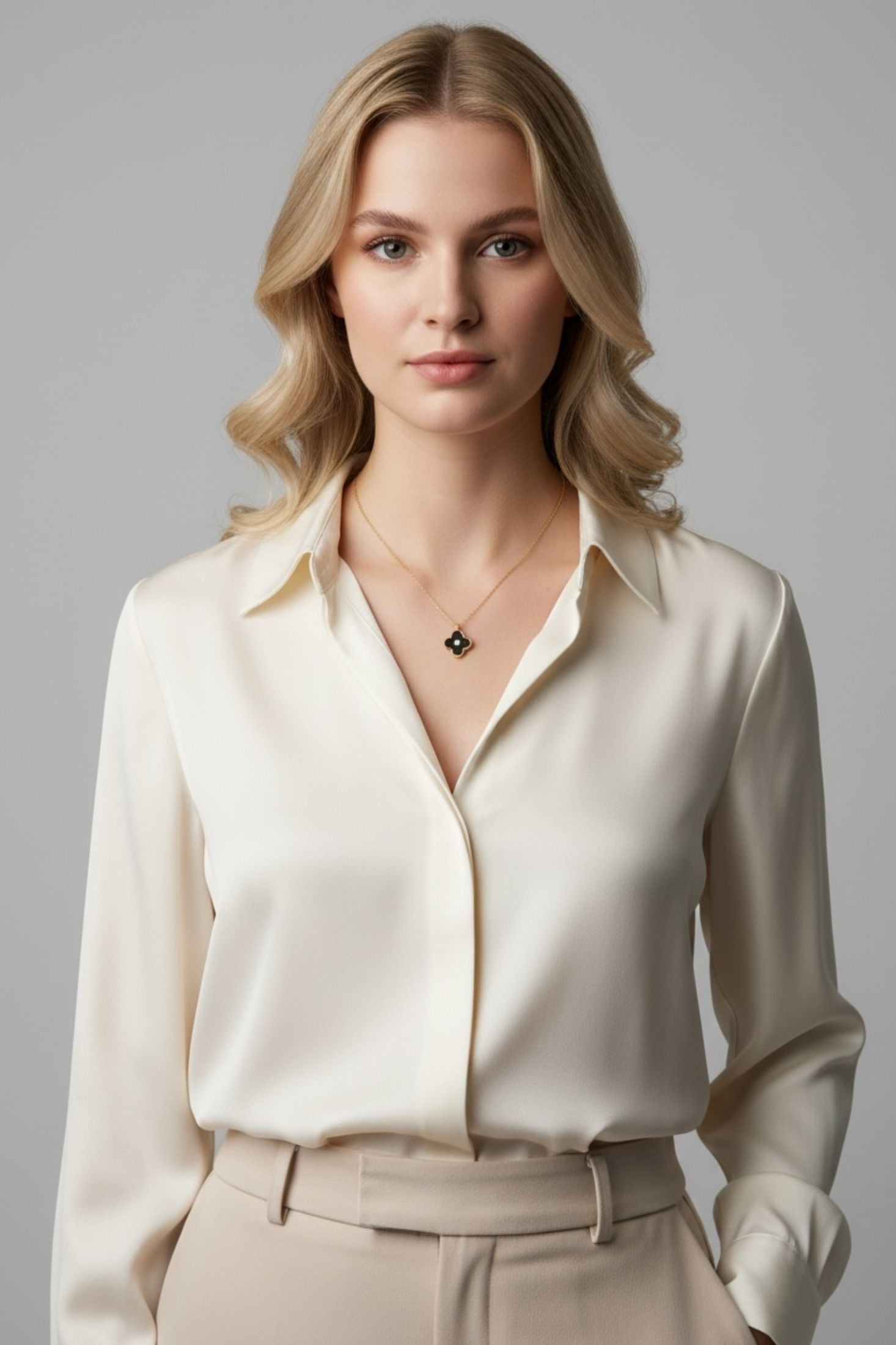 Woman wearing a white blouse and gold necklace with a black clover pendant on a gray background