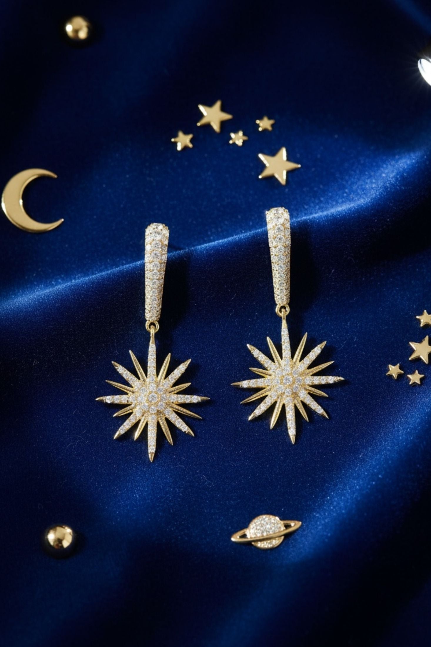 Gold star-shaped earrings on a blue satin background with celestial decorations.