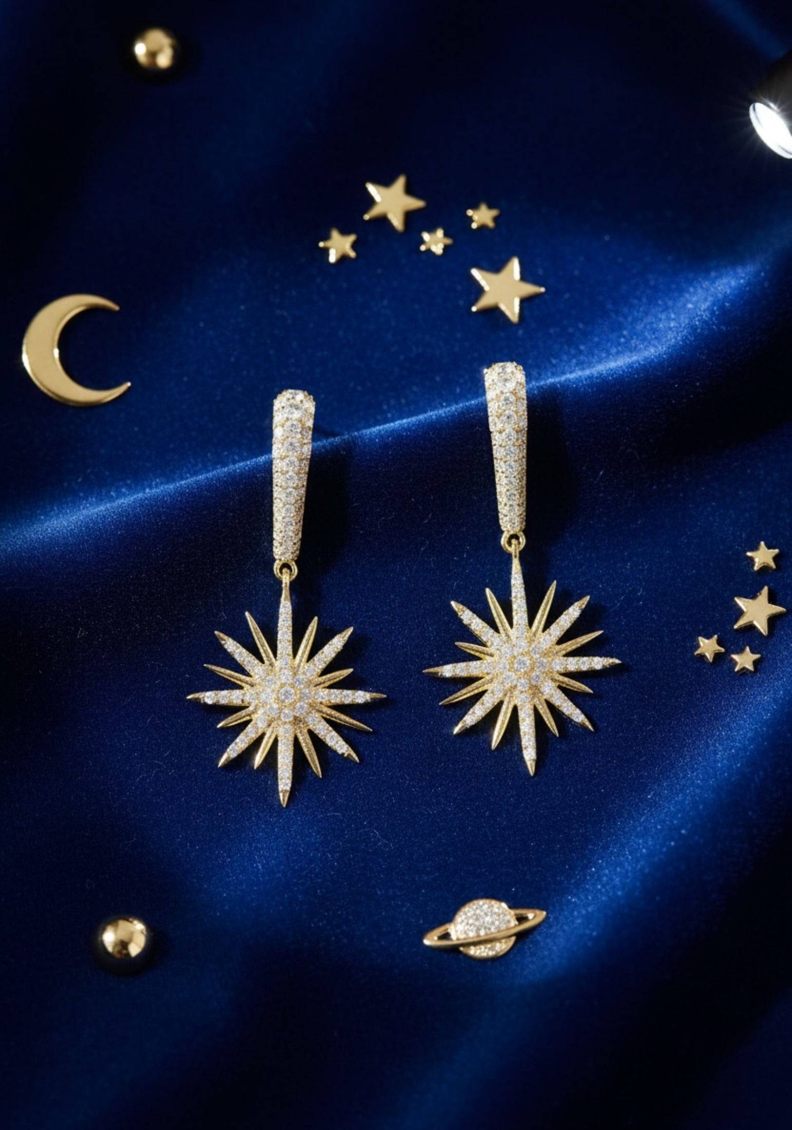 Gold star-shaped earrings on a blue satin background with celestial decorations.