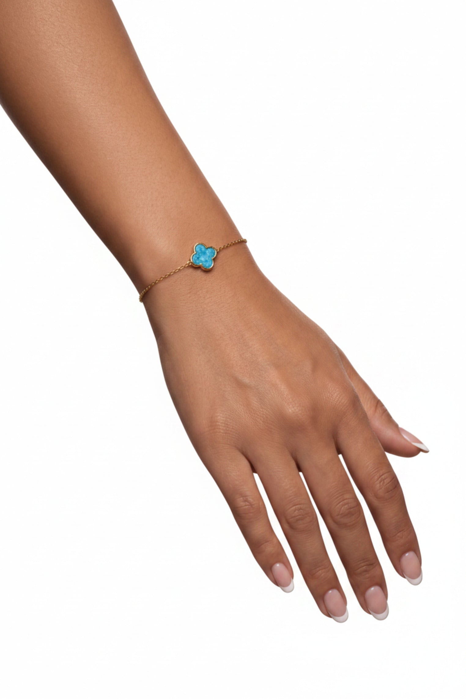 A delicate gold-tone bracelet with a small blue flower charm, worn on a model's wrist resting on a textured gray block.