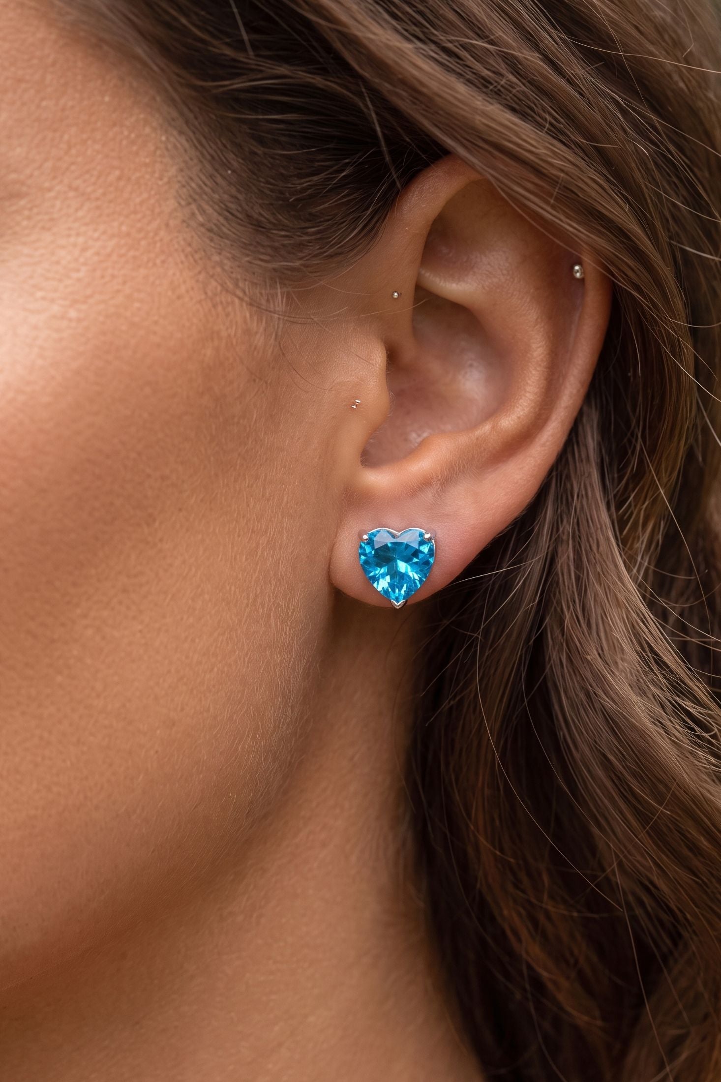 Angled view of Amore Heart Blue Topaz Stud Earrings Silver, showing heart design, blue topaz detailing, silver finish and the jewellery profile.