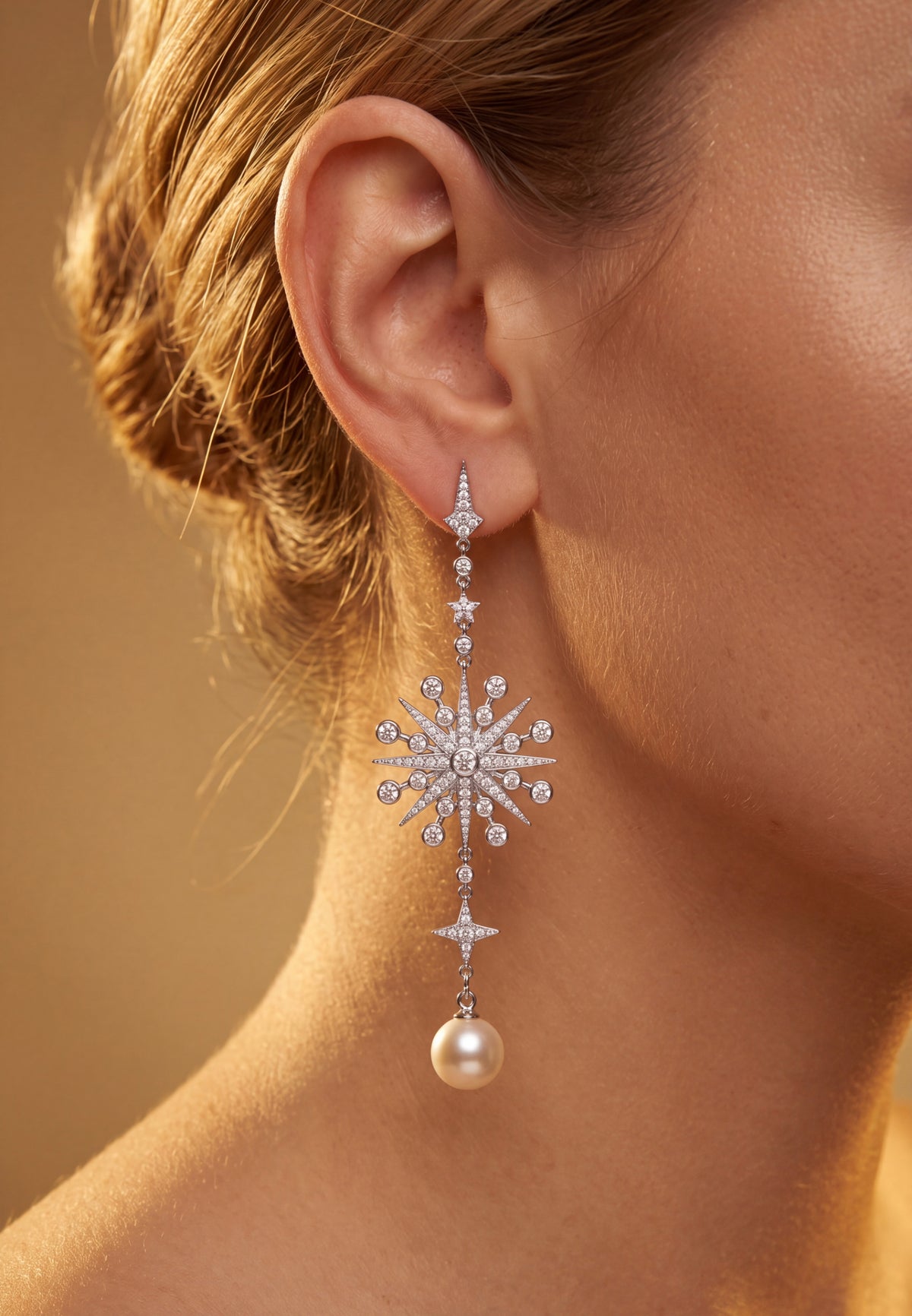 Woman wearing a long diamond starburst drop earring with a pearl pendant