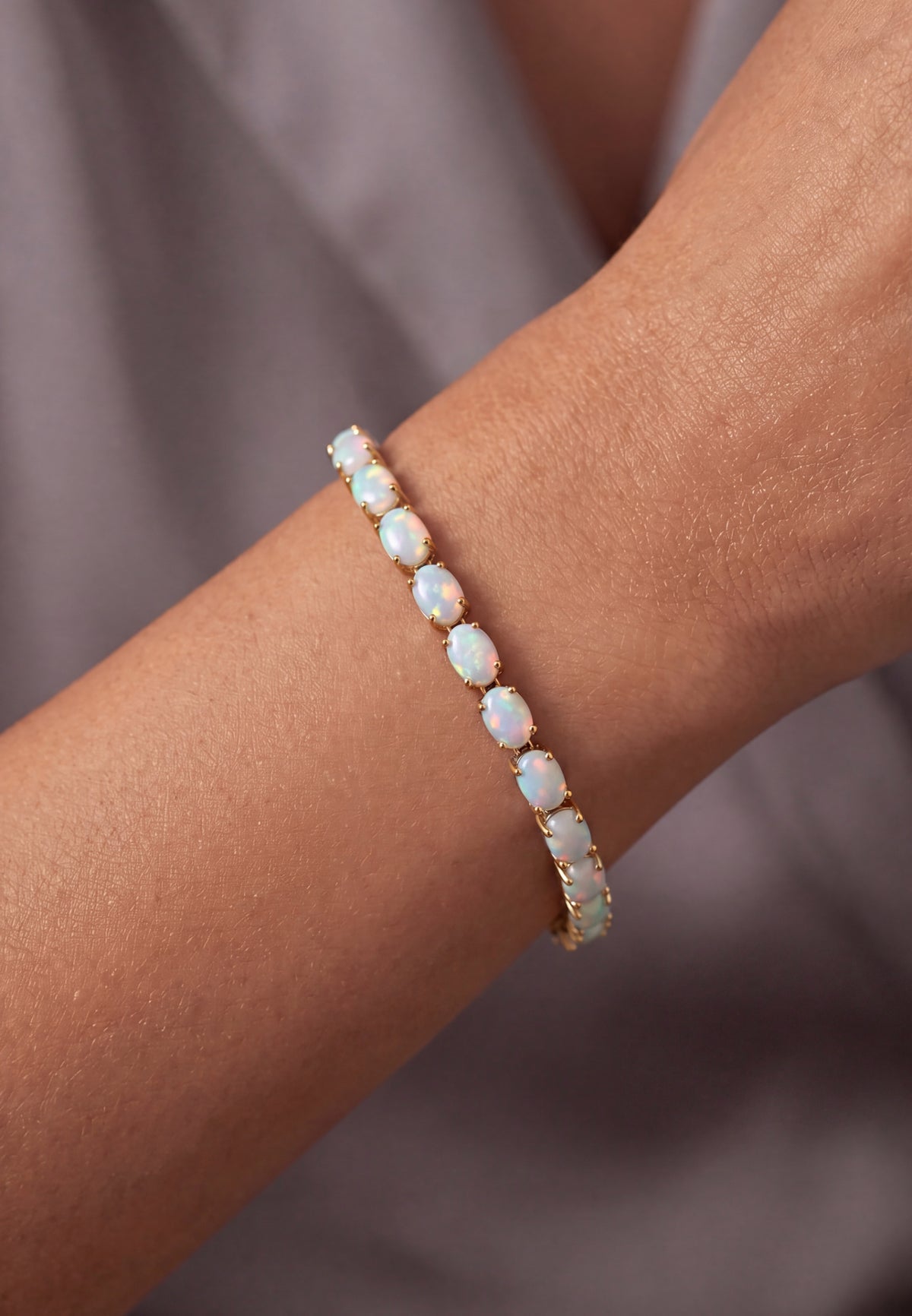 Close-up of a woman's wrist wearing a gold bracelet with oval white opals.