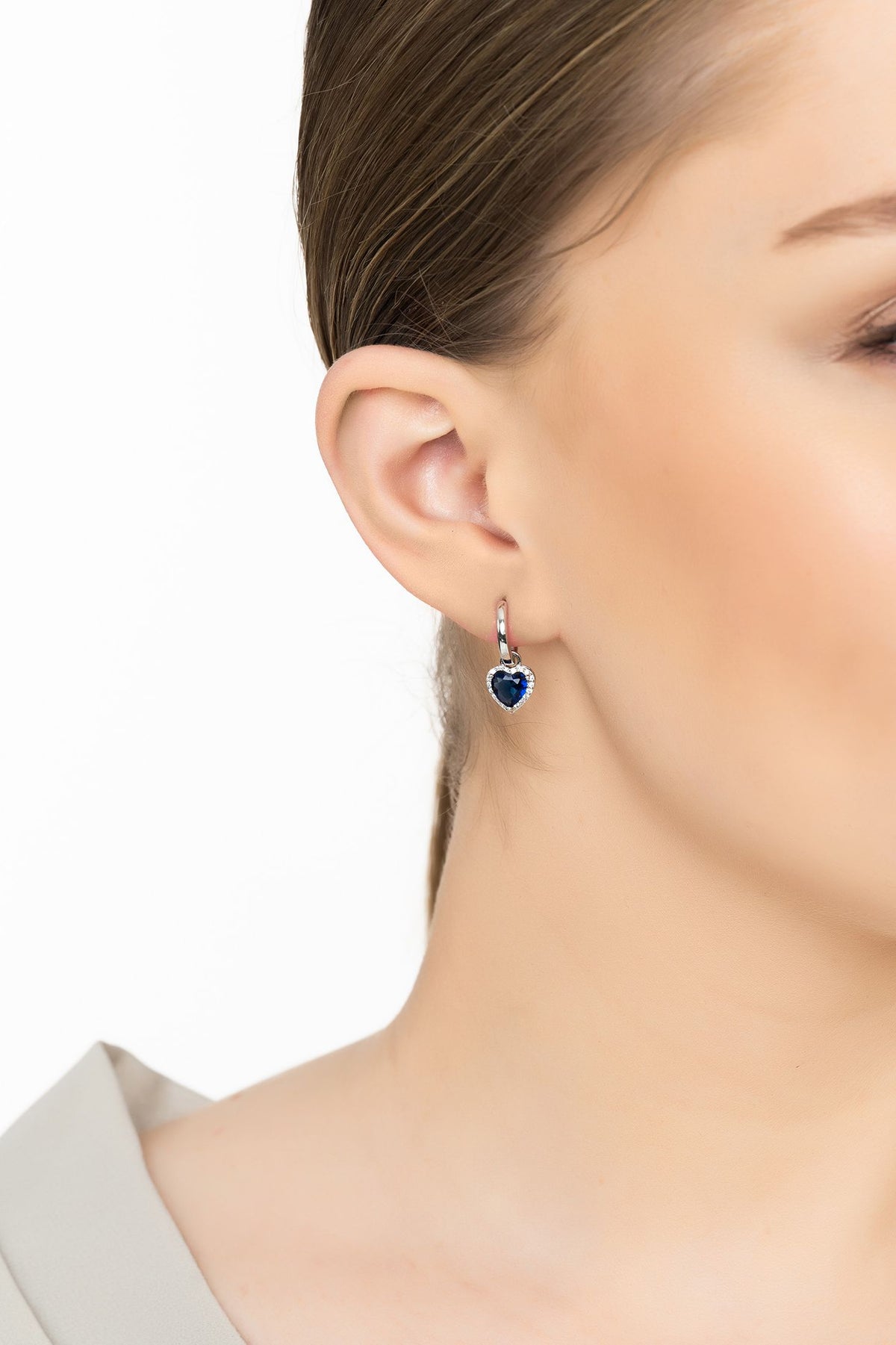 Angled view of Cupids Sparkle Sapphire Heart Drop Earrings Silver, showing heart design, sapphire detailing, silver finish and the jewellery profile.