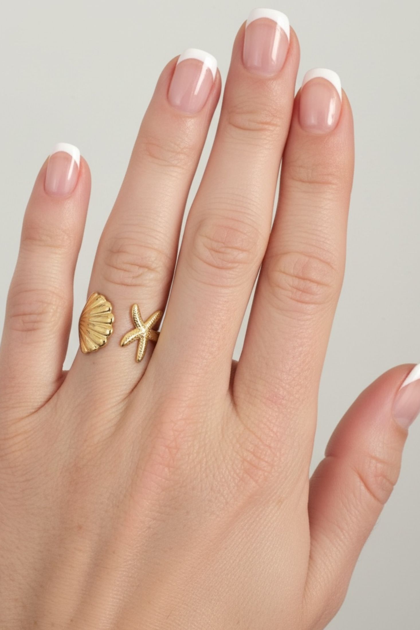 Hand wearing a gold ring with shell and starfish designs on a neutral background