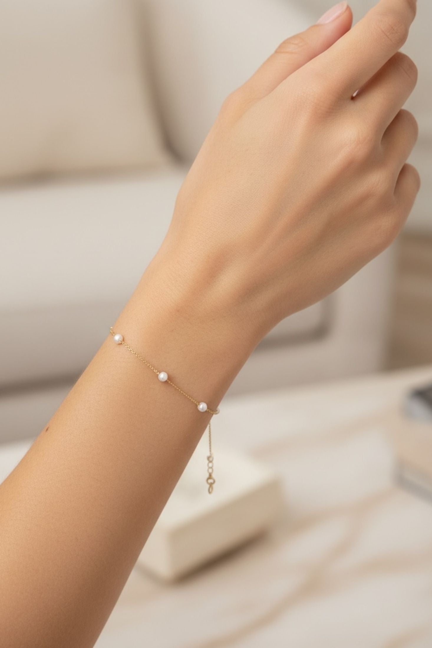 Hand wearing a delicate bracelet with small pearls on a neutral background