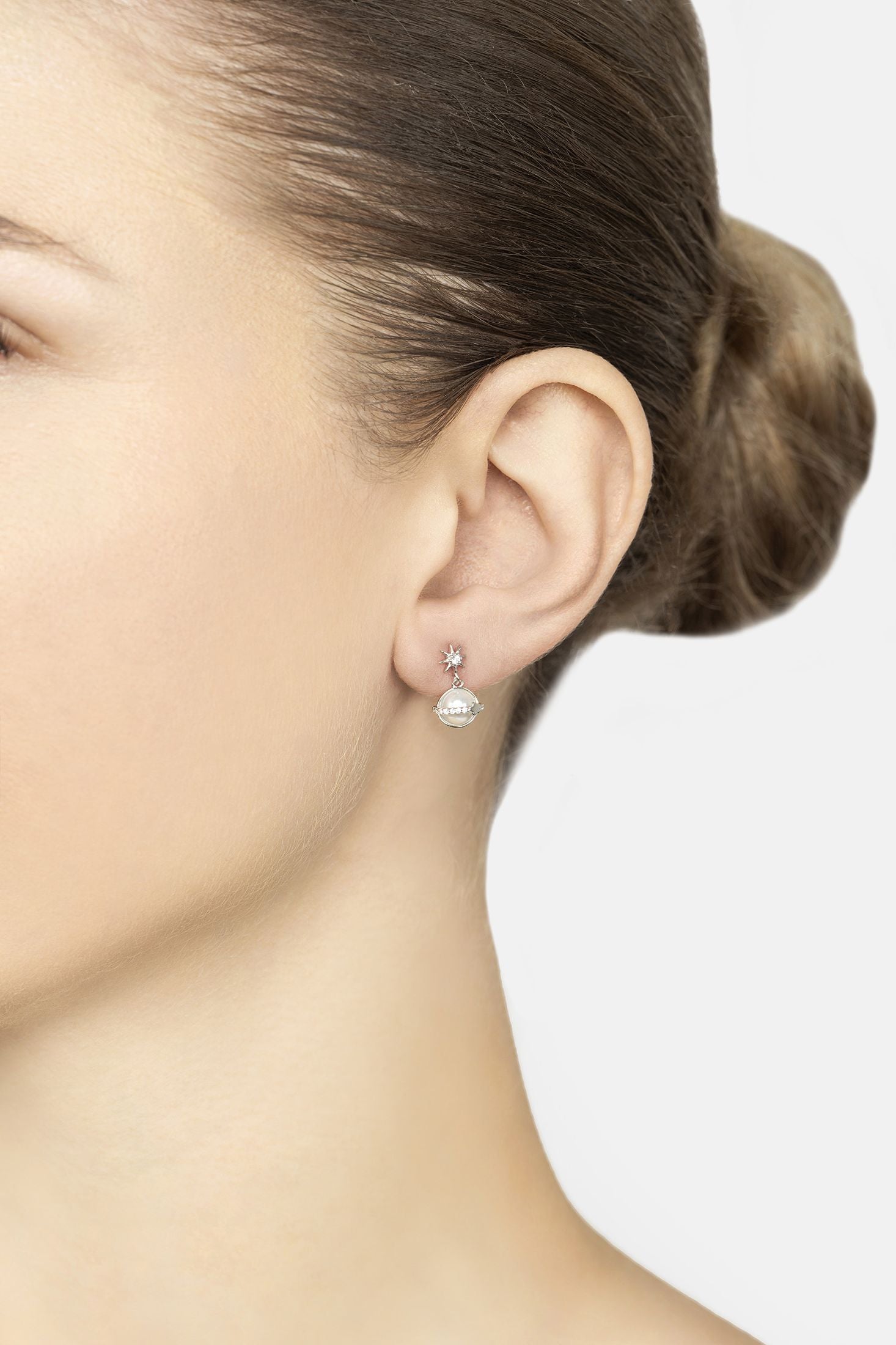 Close-up of a person wearing pearl earrings with a plain background