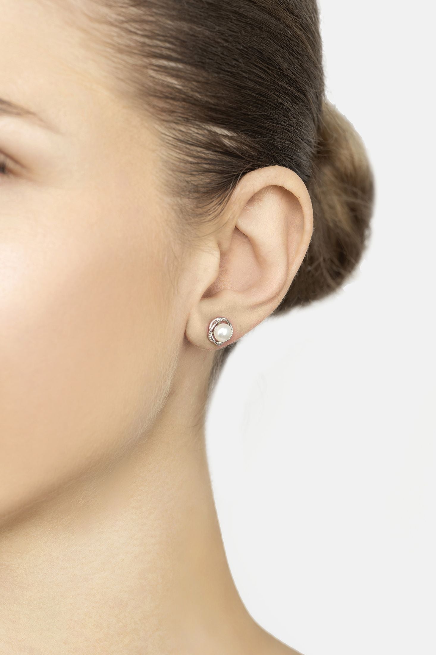 Close-up of a person wearing a pearl stud earring on a plain background