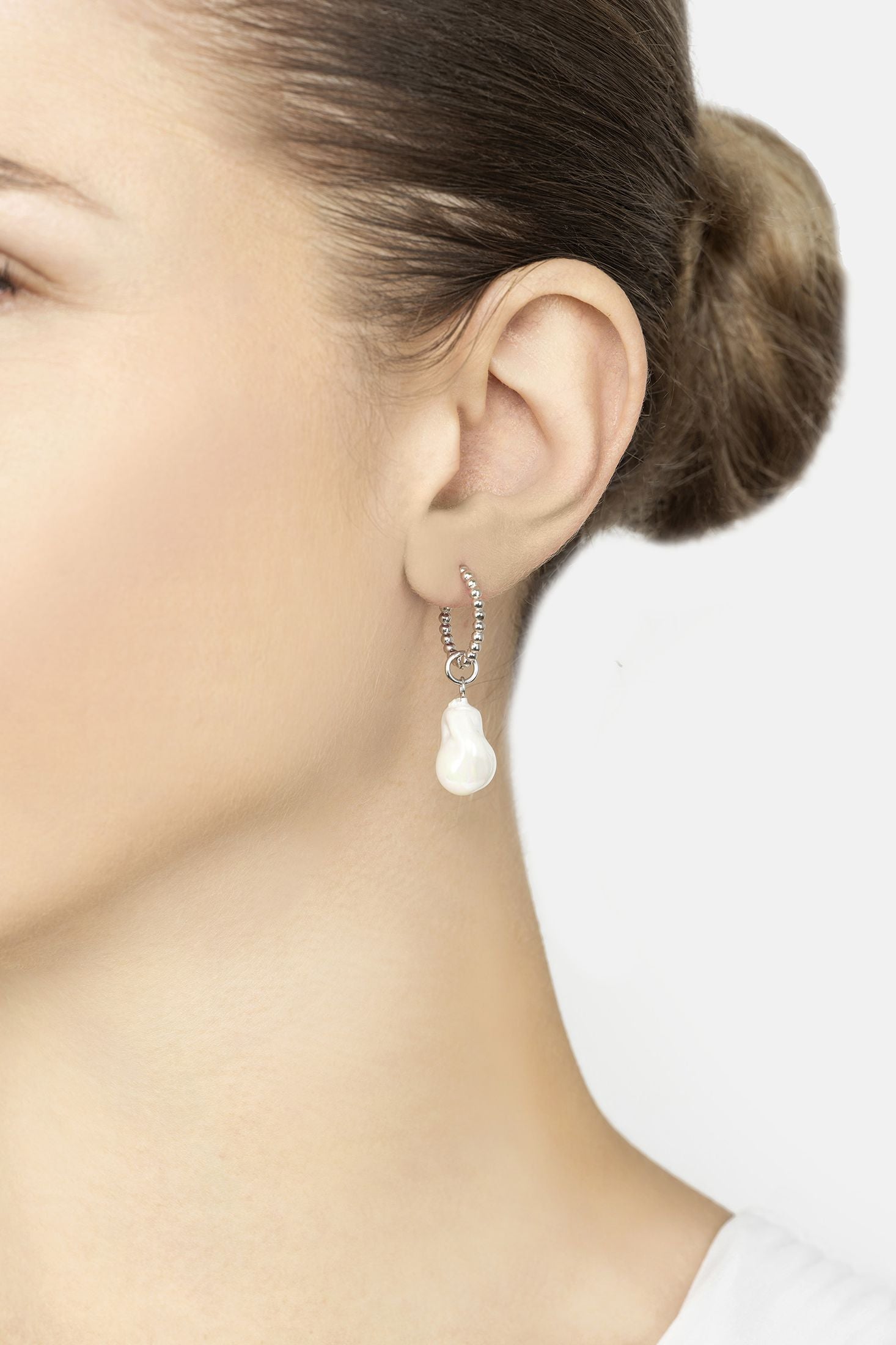 Pearl earring worn by a person on a plain background
