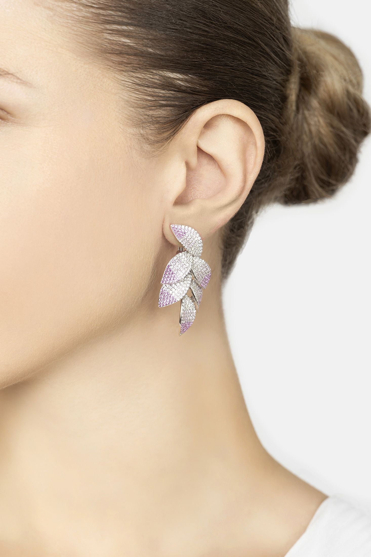 Close-up of a person wearing a leaf-shaped earring with pink and purple stones on a white background