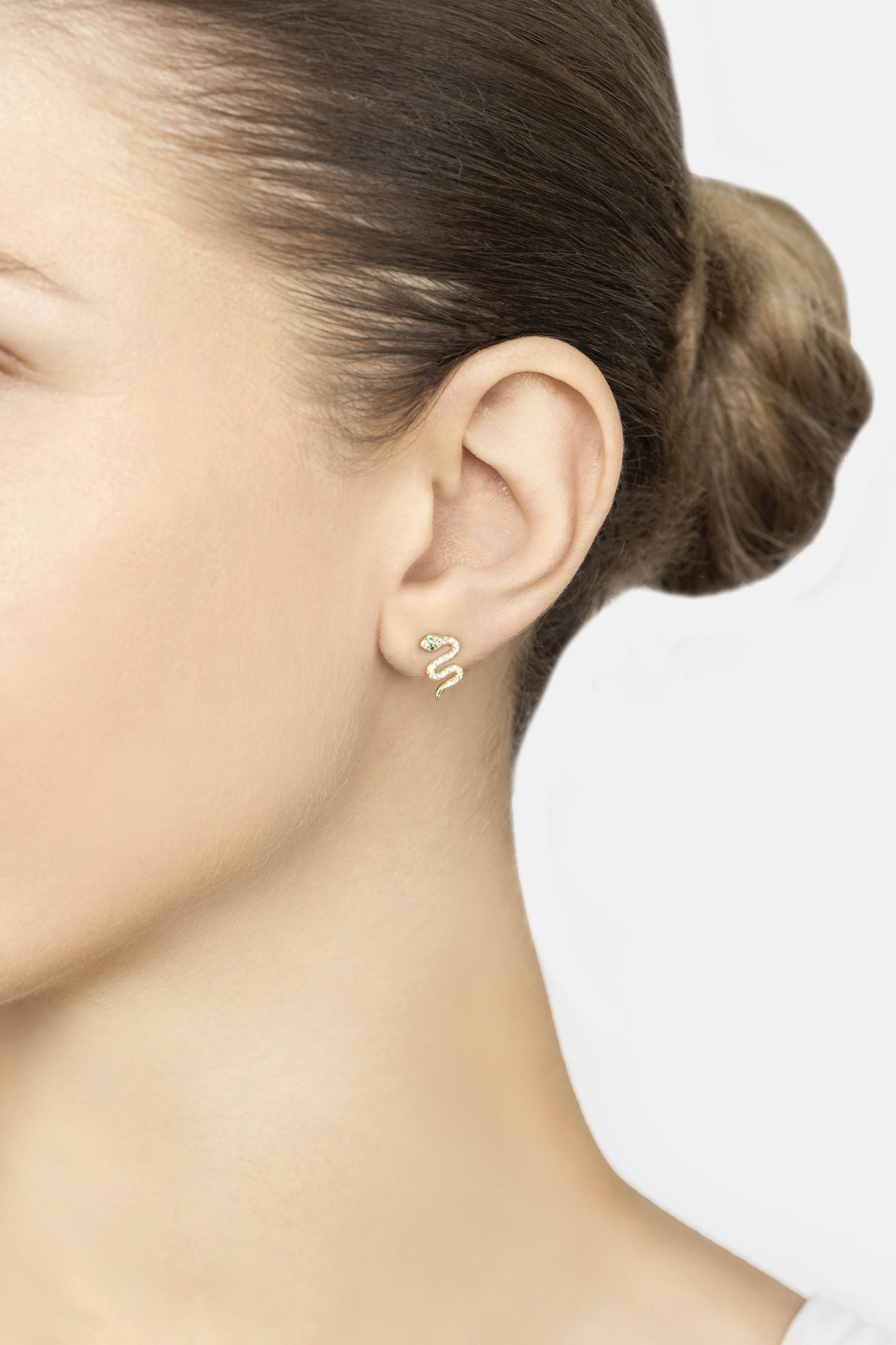 Close-up of a person wearing gold snake-shaped earrings with a plain background