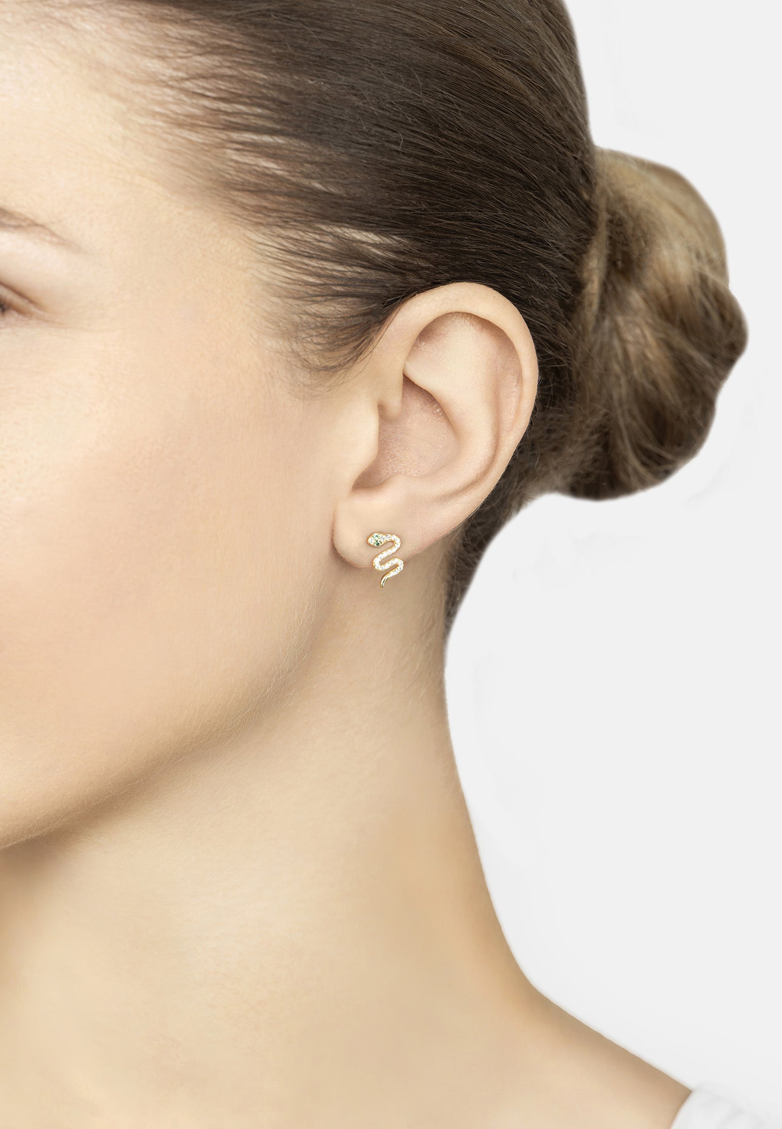 Close-up of a person wearing gold snake-shaped earrings with a plain background