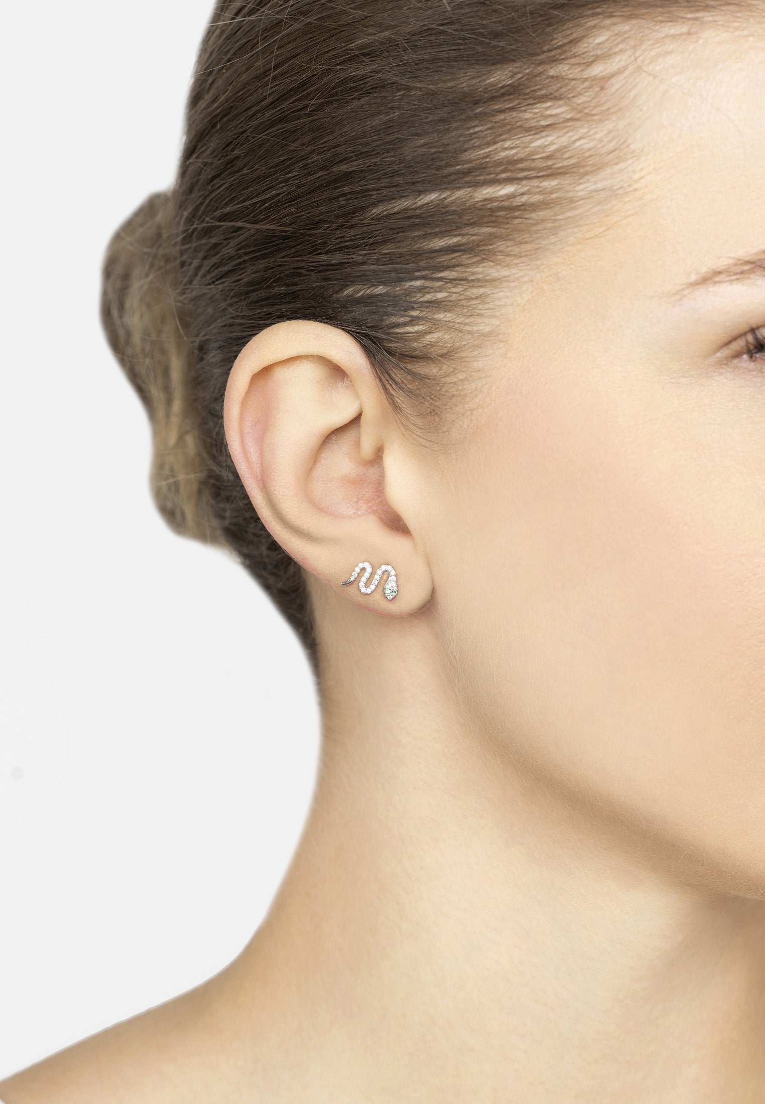 Close-up of a person wearing a snake-shaped earring on a plain background