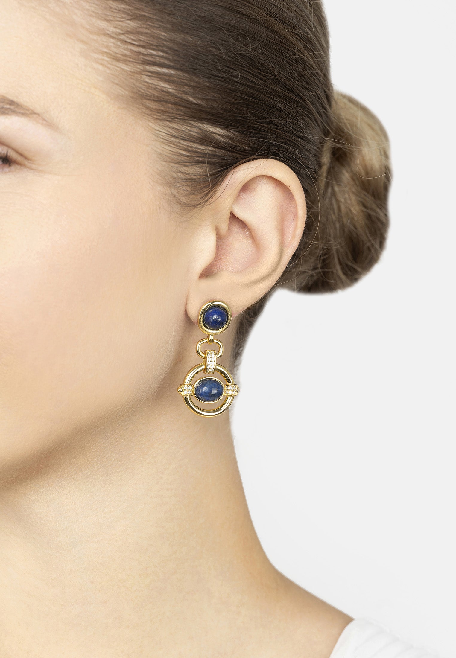 Close-up of a person wearing gold earrings with blue stones on a white background