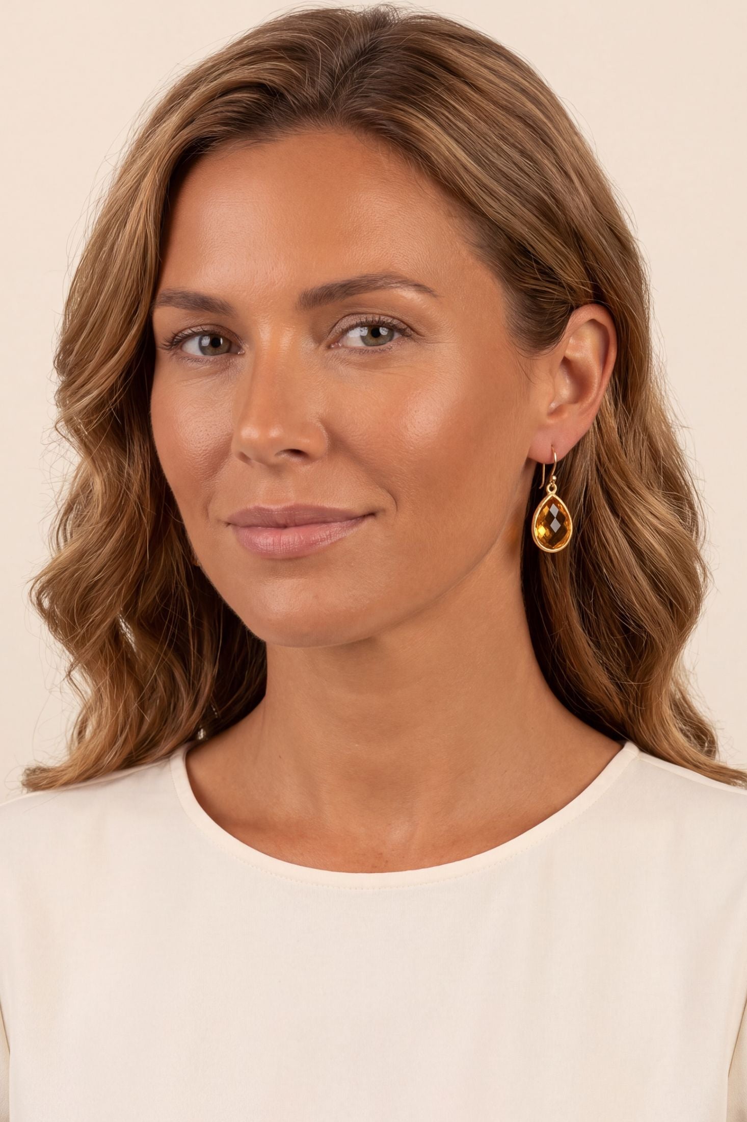 Woman wearing elegant gold drop earrings with amber teardrop gemstone, hypoallergenic and sustainably made.