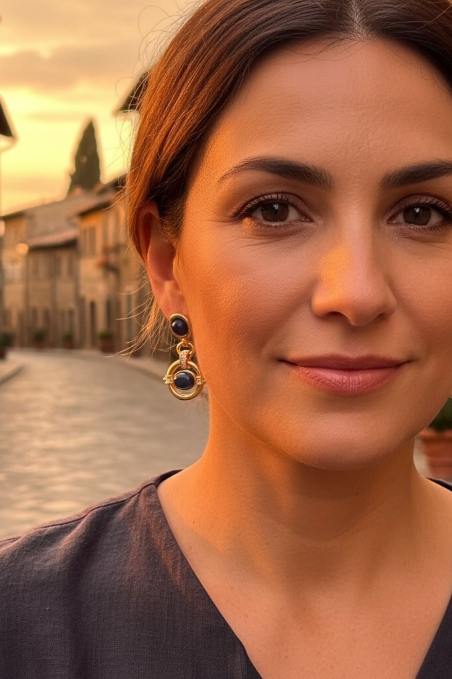 Woman with earrings standing in a street wearing gold earrings with blue gemstones