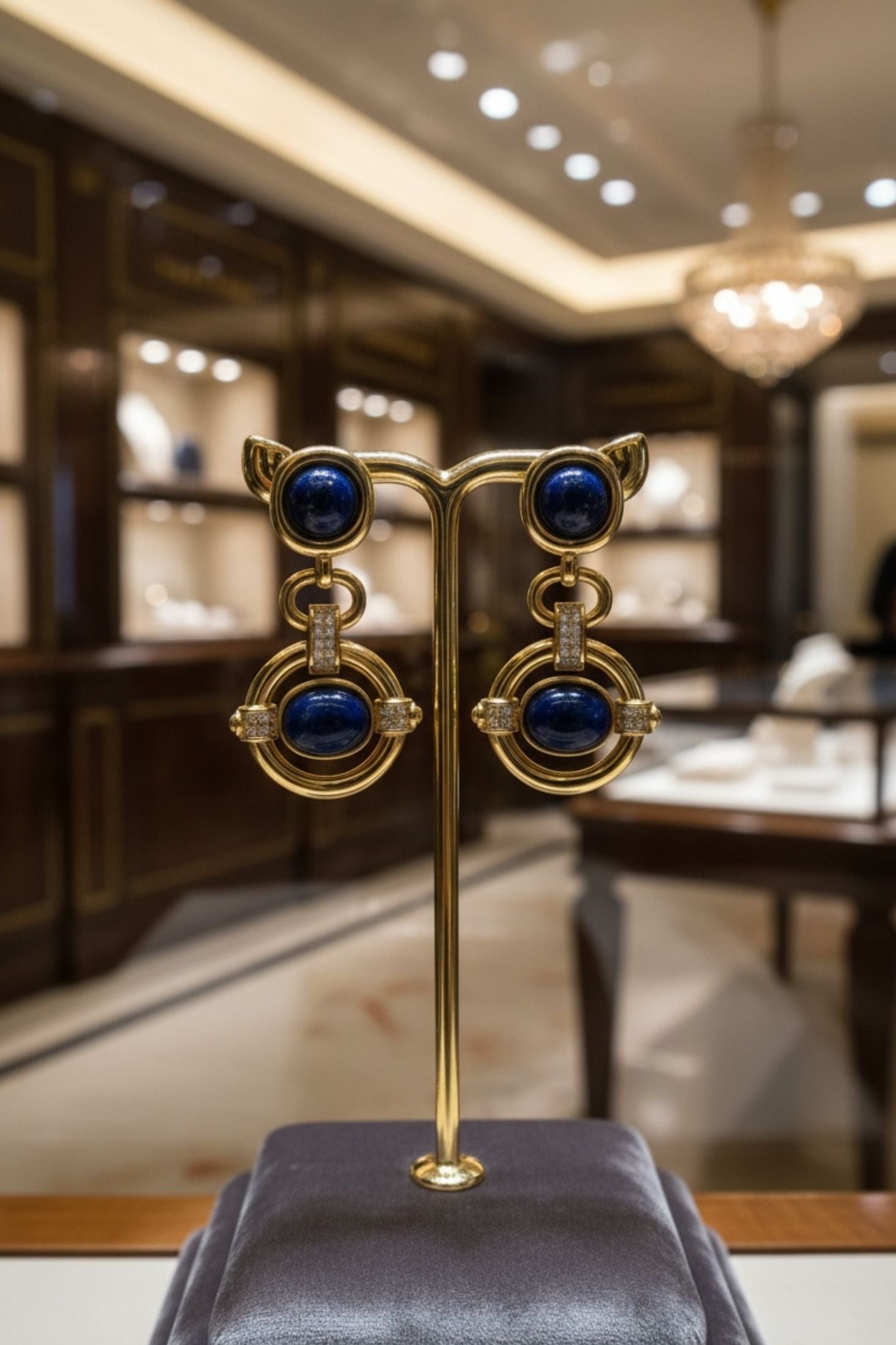 Gold earrings with blue stones on a stand in a blurred interior setting