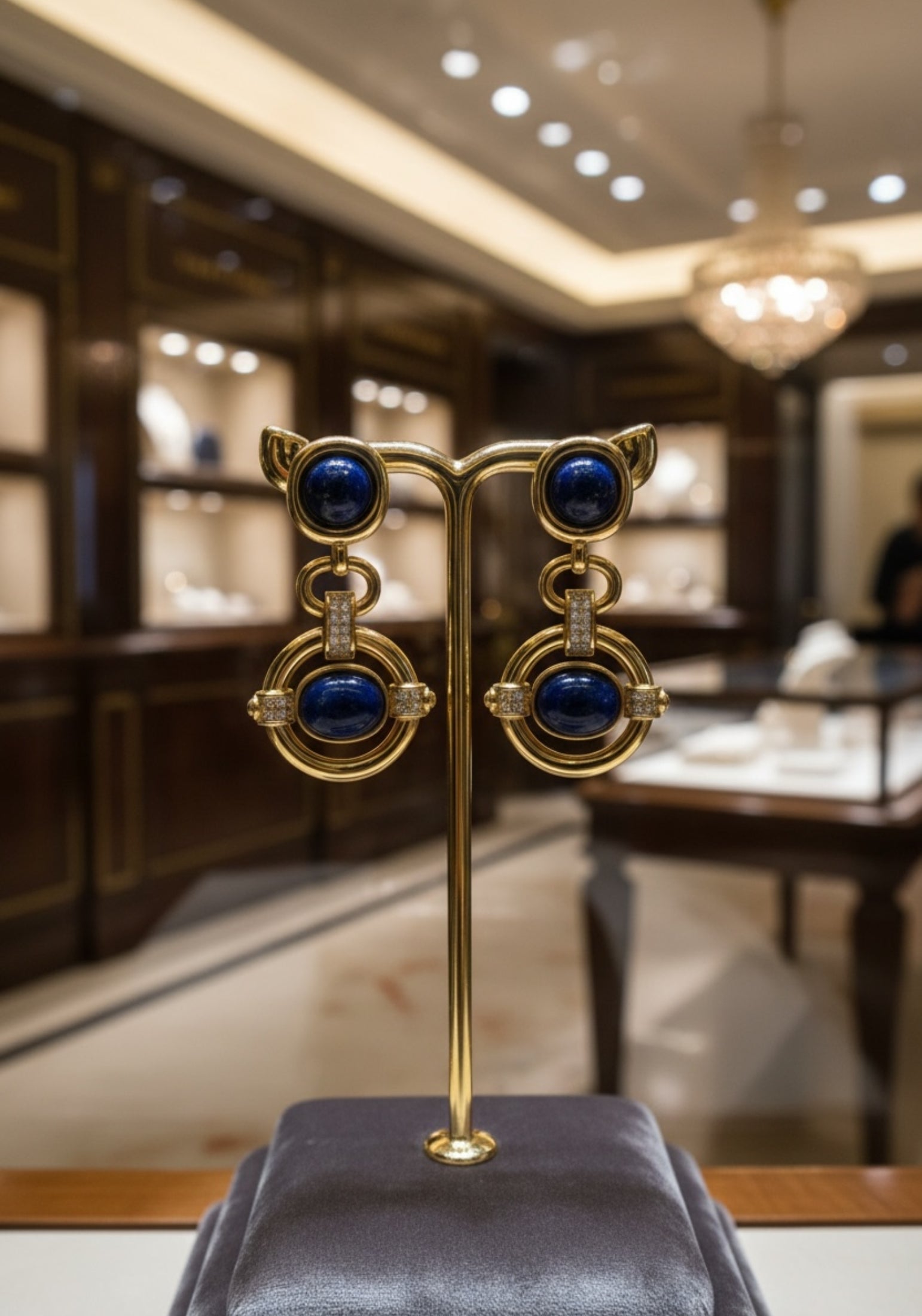 Gold earrings with blue stones on a stand in a blurred interior setting