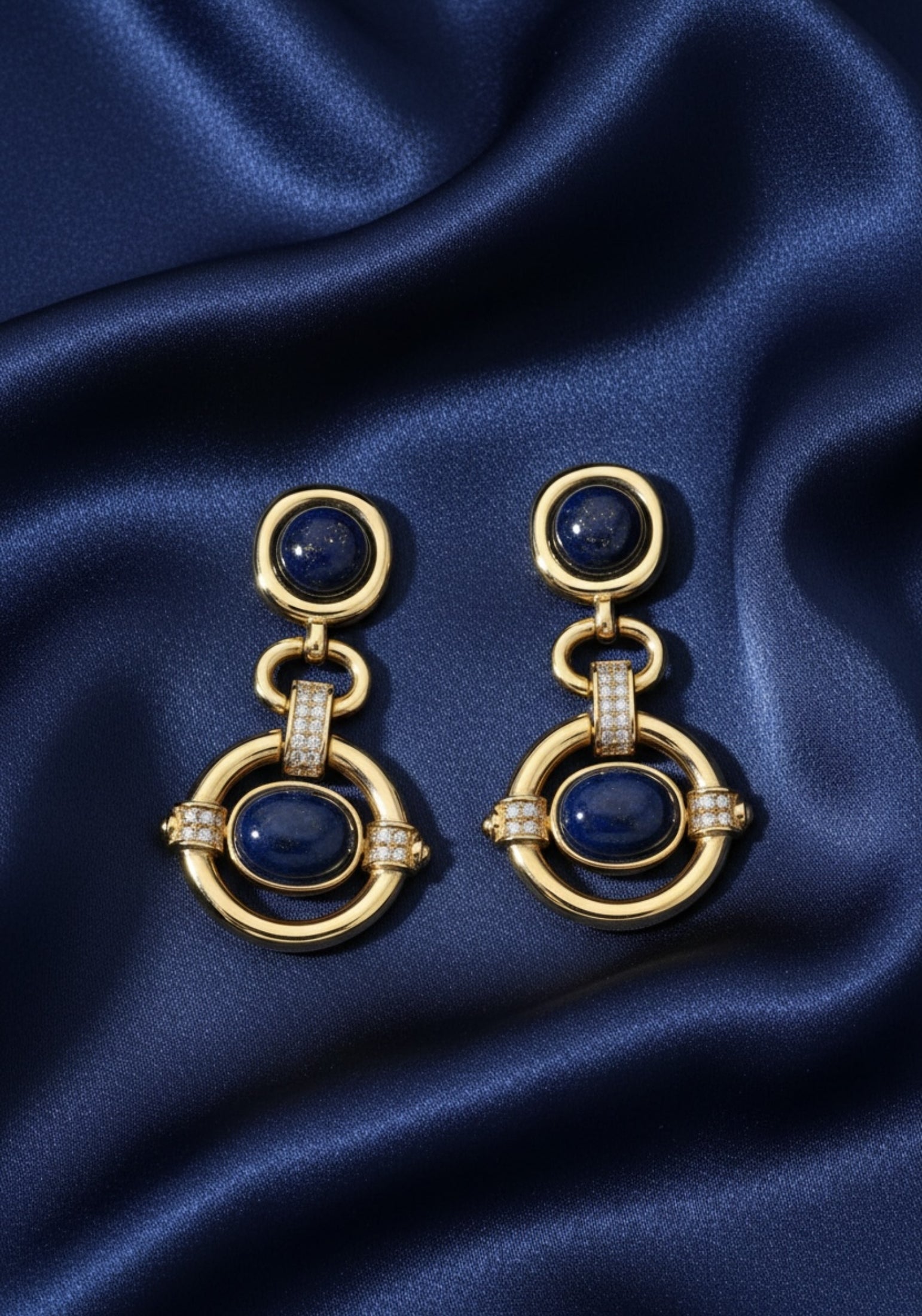 Gold earrings with blue stones on a blue satin background