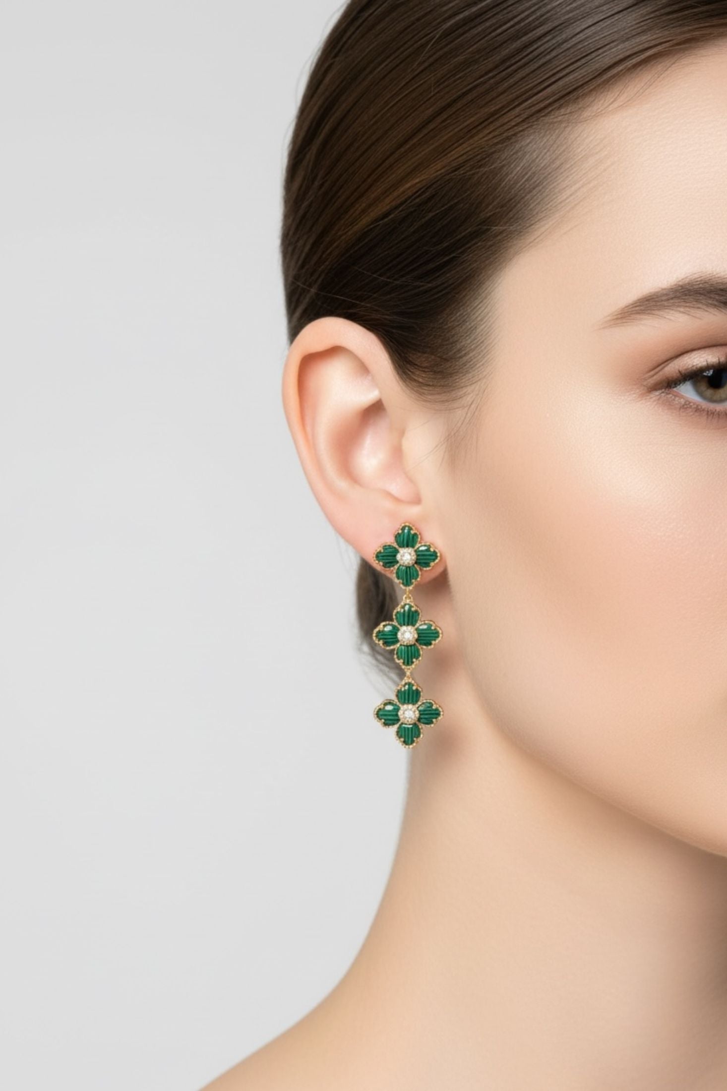 Close-up of a person wearing green emerald earrings on a plain background