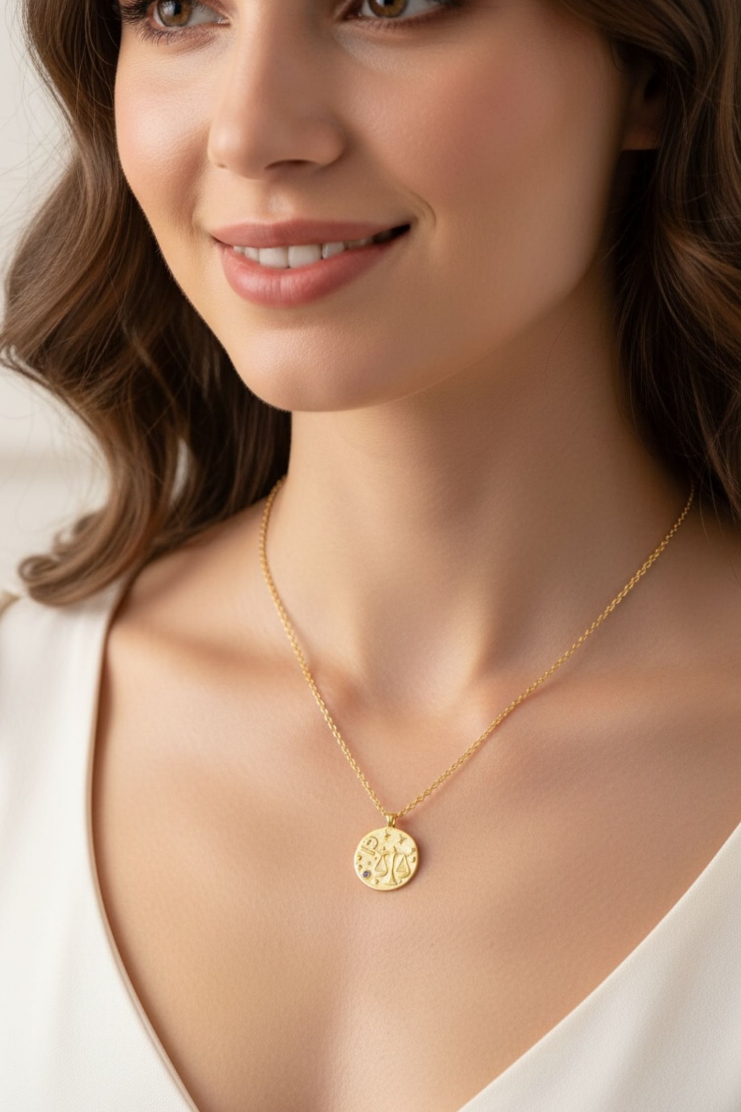 Woman wearing a gold necklace with a circular pendant on a neutral background