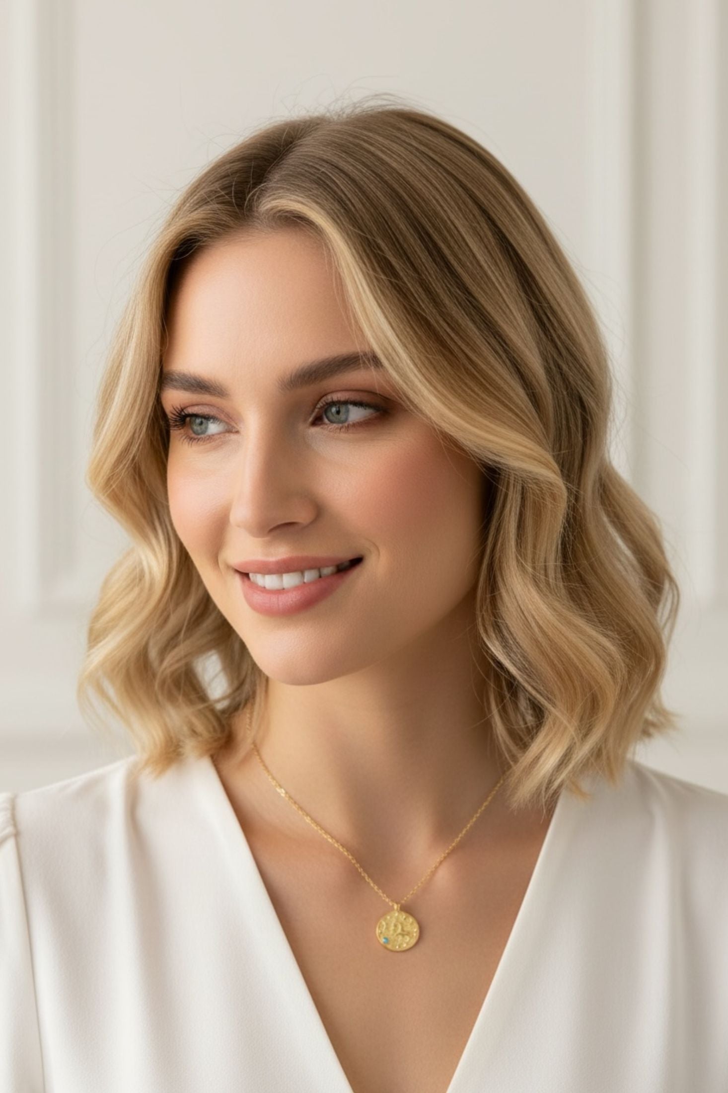 Woman wearing a gold necklace with a circular pendant against a plain background
