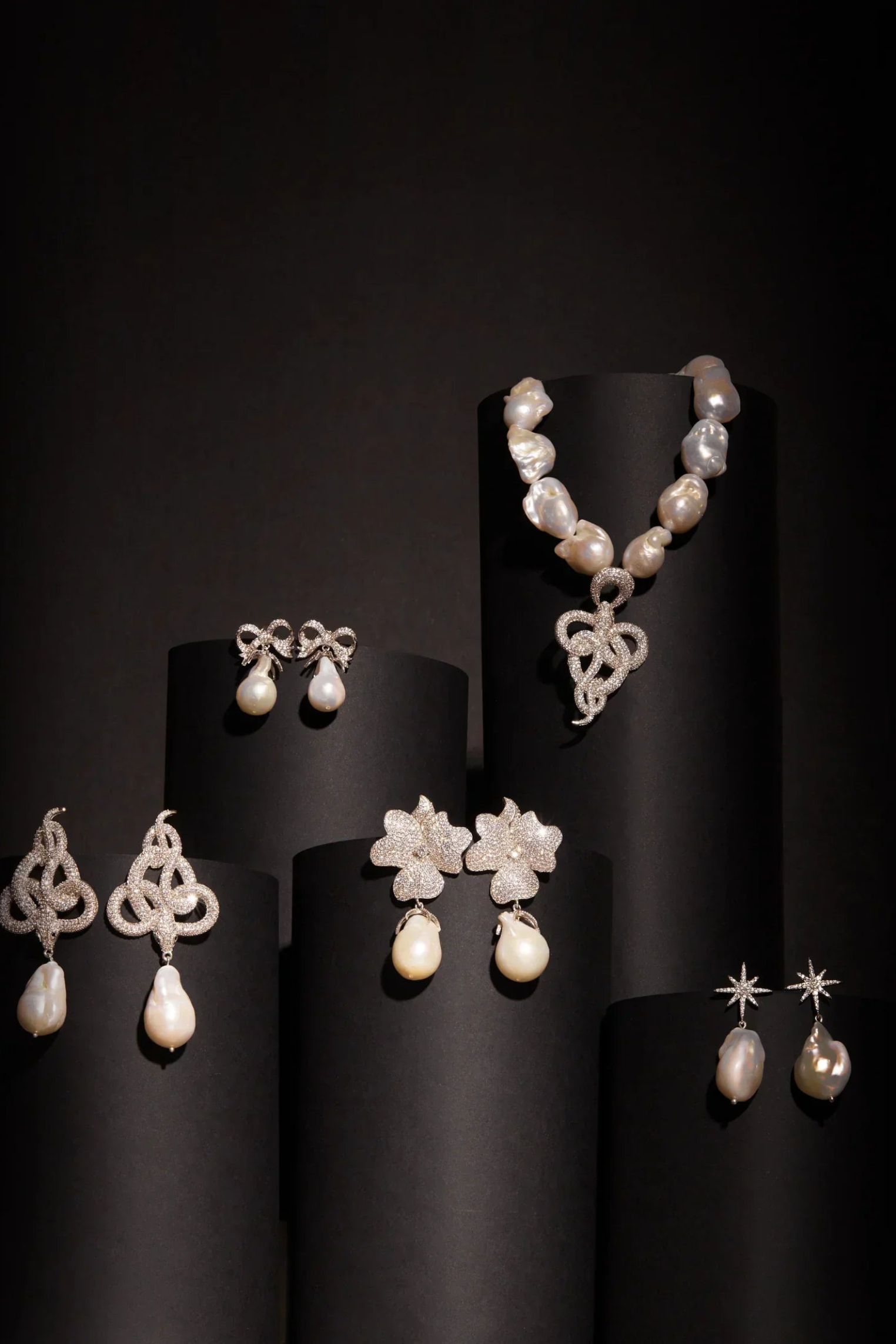 Pearl jewelry set including necklace and earrings on black stands against a dark background